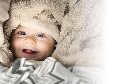 Smiling baby wrapped in a soft, cream-colored blanket with a textured pattern, conveying warmth and comfort