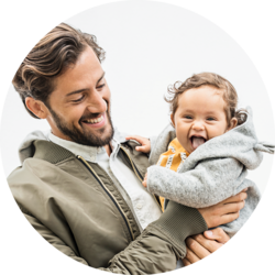 Smiling father holding a joyful baby dressed in a gray hoodie.