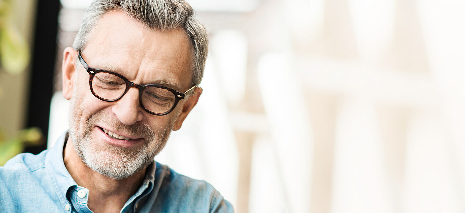 A close-up of an older man wearing glasses, smiling gently and looking down.